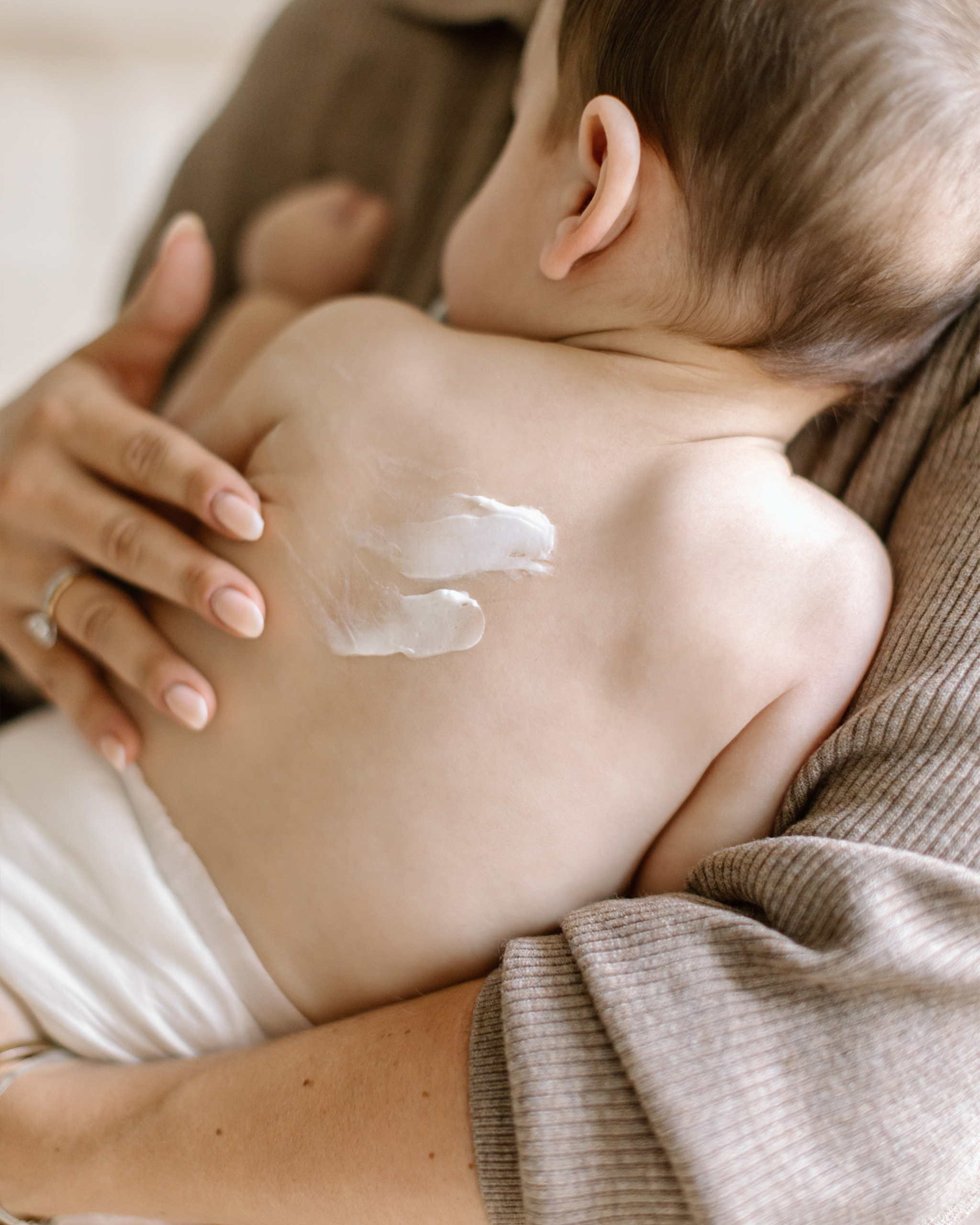 A mom massaging My Petite Coco baby cream onto her baby's skin.