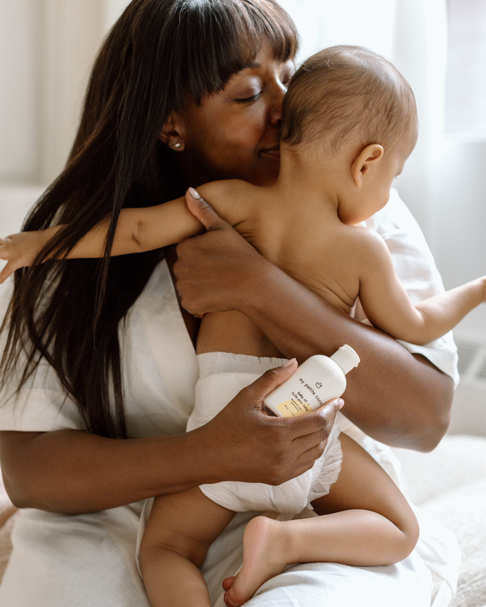 Mom holding My Petite Coco baby oil with alongside her baby.